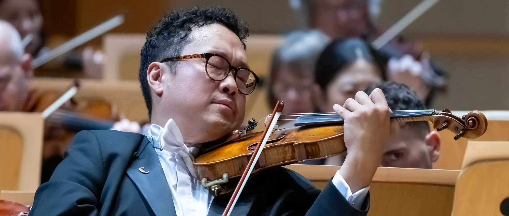 Dennis Kim playing his violin with closed eyes in front of Pacific Sym