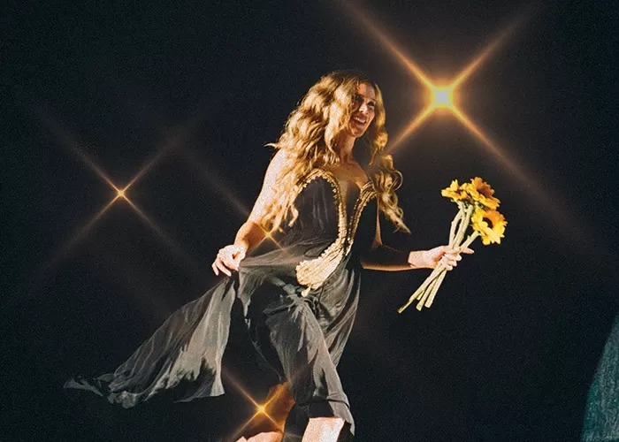 Joss Stone in a sparkling dress wih her arm up in the air in front of an audience