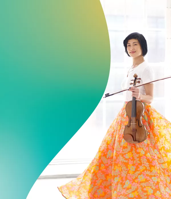 Jennifer Koh in a white blouse and colorful skirt holding her violin