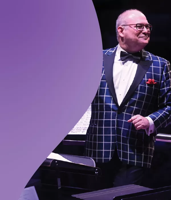 Guest conductor Stuart Chafetz wearing a plaid jacket and smiling while he conducts