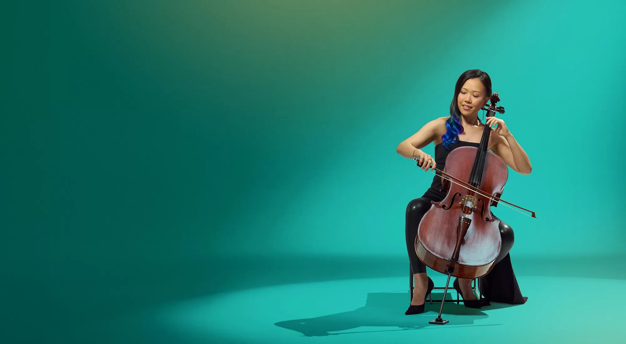 Young woman in black playing a cello against a green background